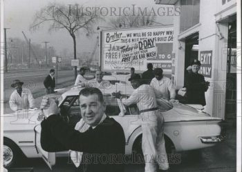 A Group Of People Standing In Front Of A Car